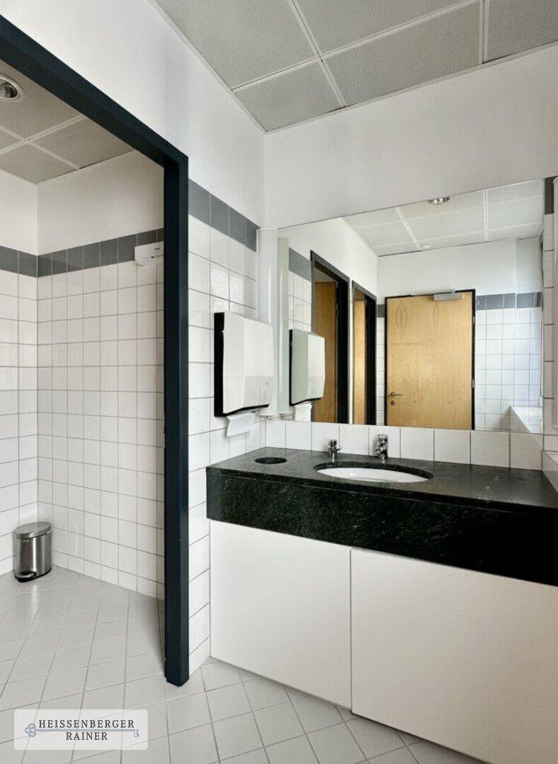 Modernes Badezimmer mit weißen Fliesen, dunkler Arbeitsplatte und großem Spiegel.