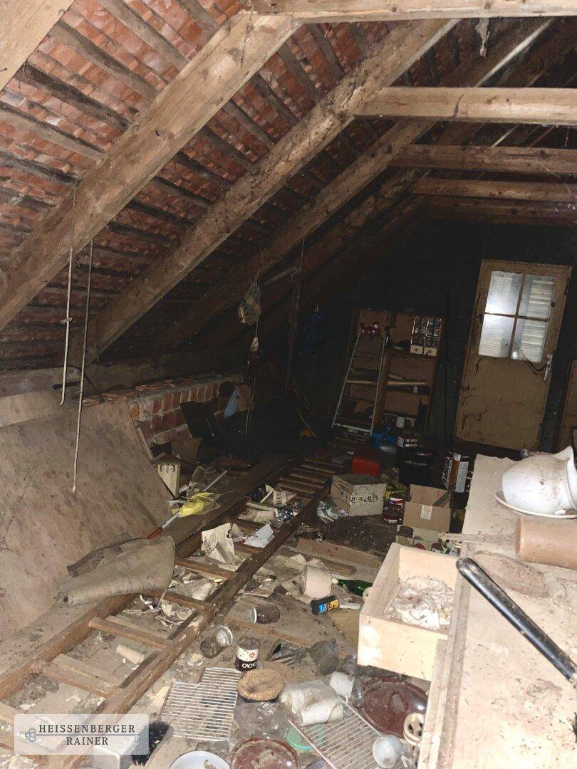 Unaufgeräumter und unfertiger Dachboden mit sichtbaren Holzbalken und viel Gerümpel.