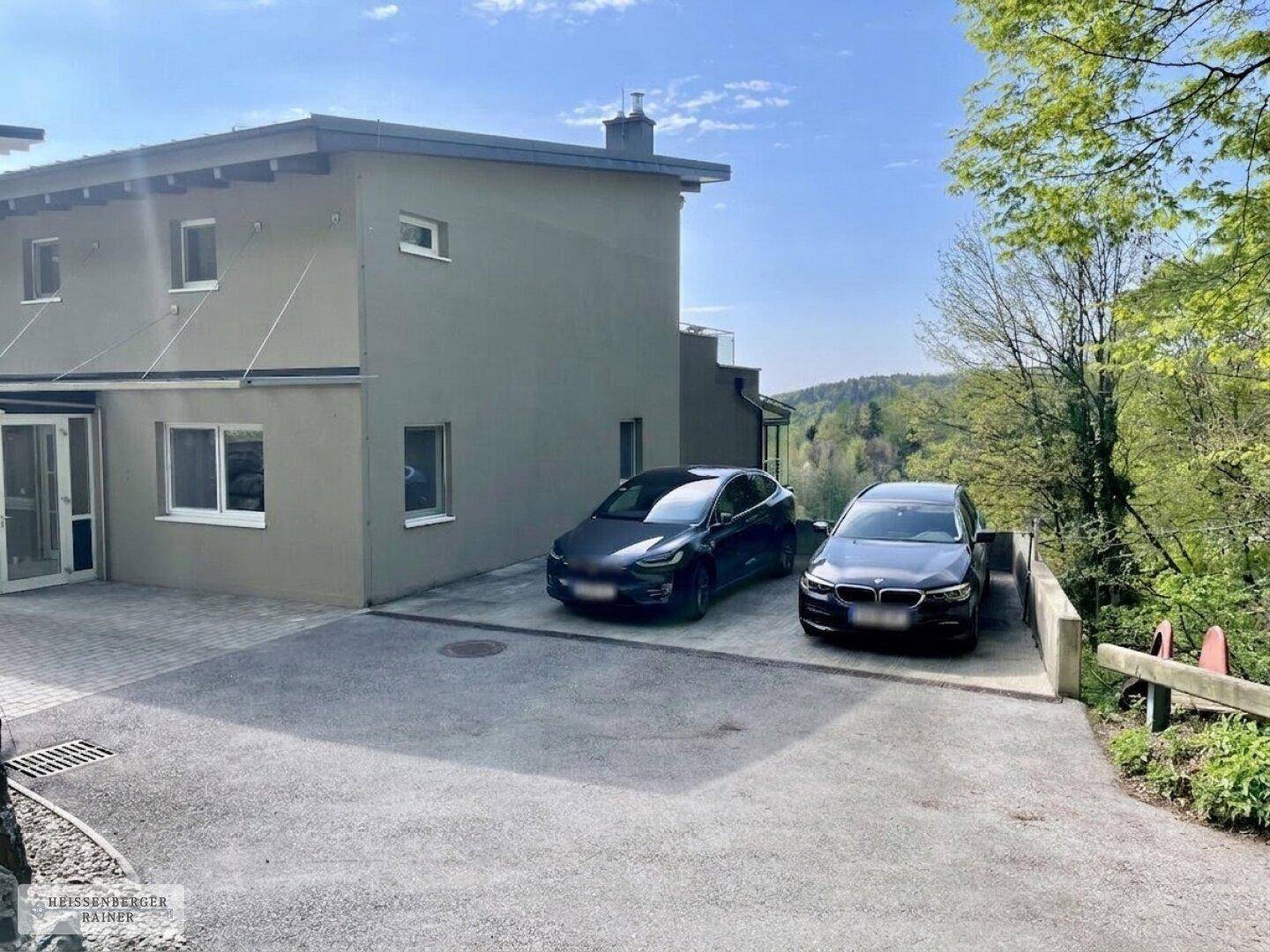 Moderne Gebäudefassade mit Parkplätzen und Zufahrt in grüner, ruhiger Umgebung.