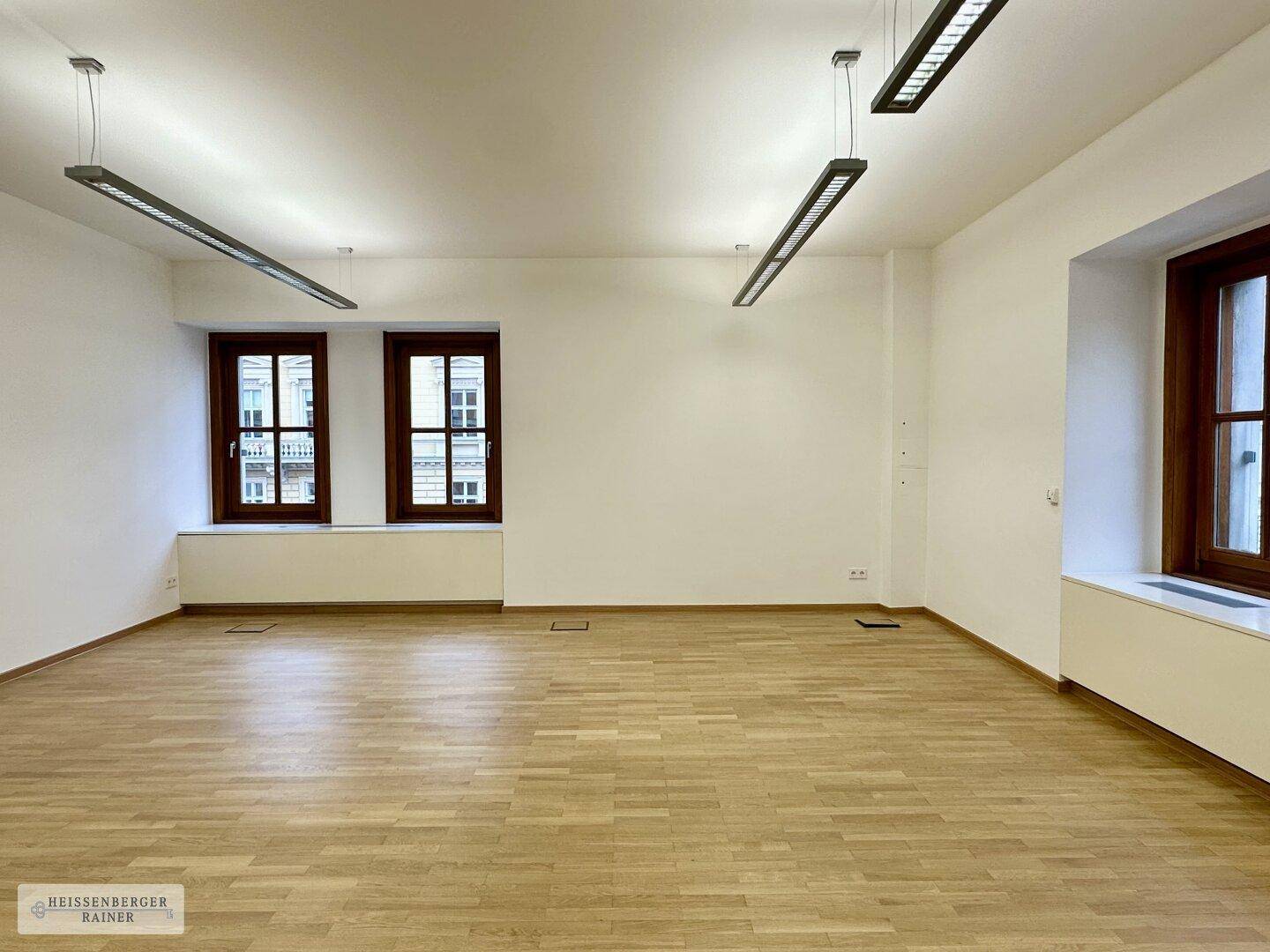Heller, leerer Büroraum mit Holzboden und großen Fenstern, ideal für flexible Arbeitsplatzlösungen.