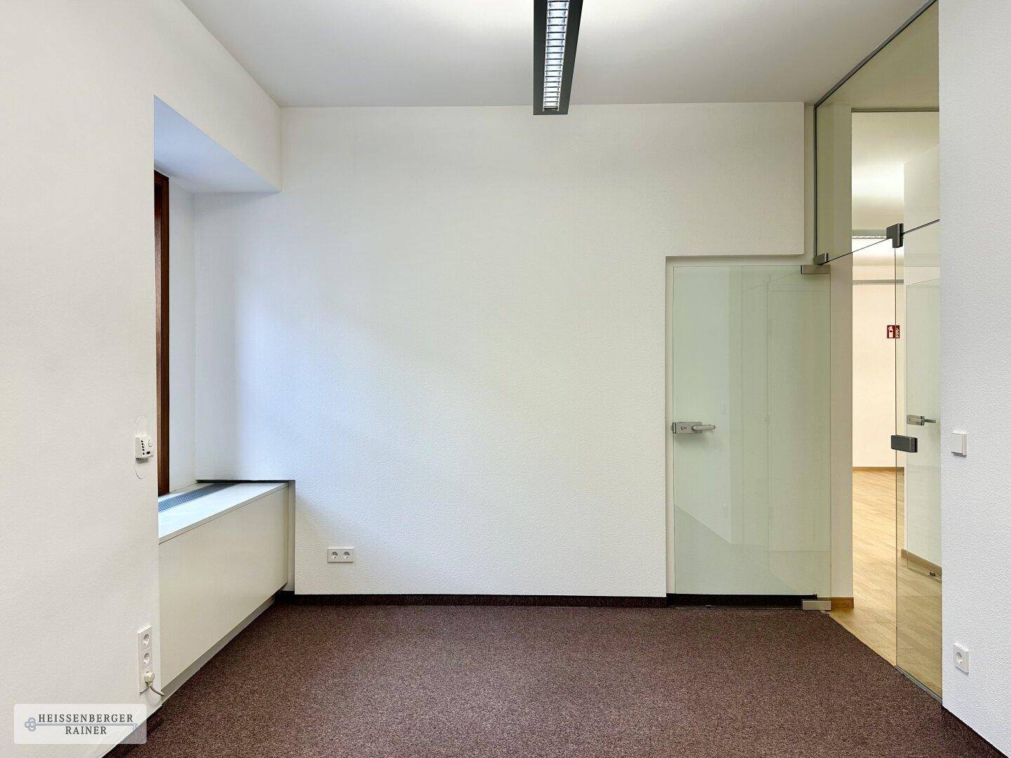 Kleiner Büroraum mit Teppichboden und Glaswand, ideal für Besprechungen oder Einzelarbeit.