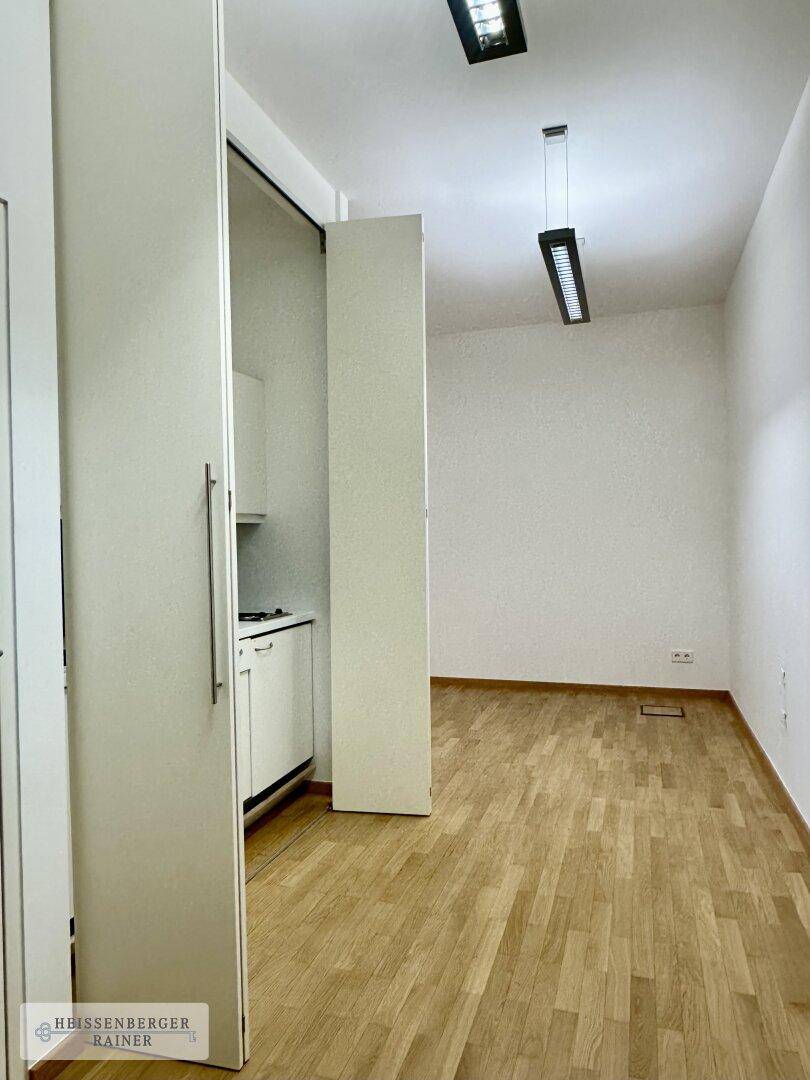 Versteckte Küchenzeile hinter Schranktüren in einem hellen Raum mit Holzboden.