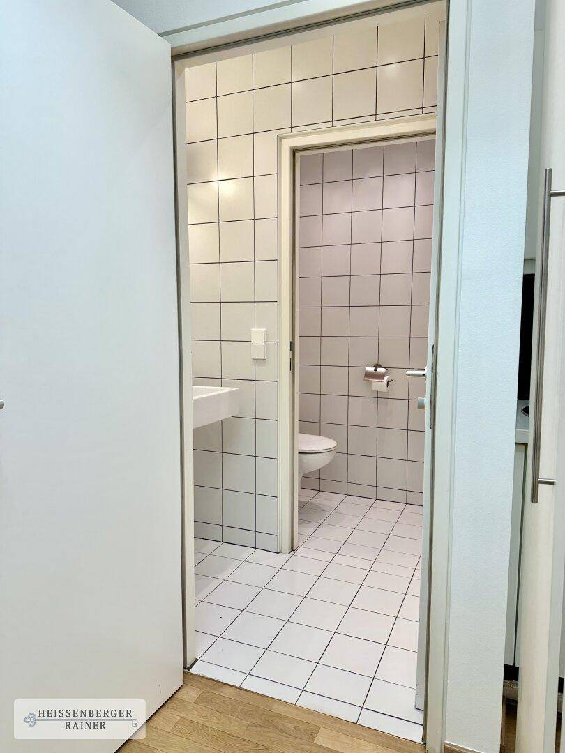 Modern gefliestes WC mit Waschbecken und Toilette, sauber und funktional gestaltet.