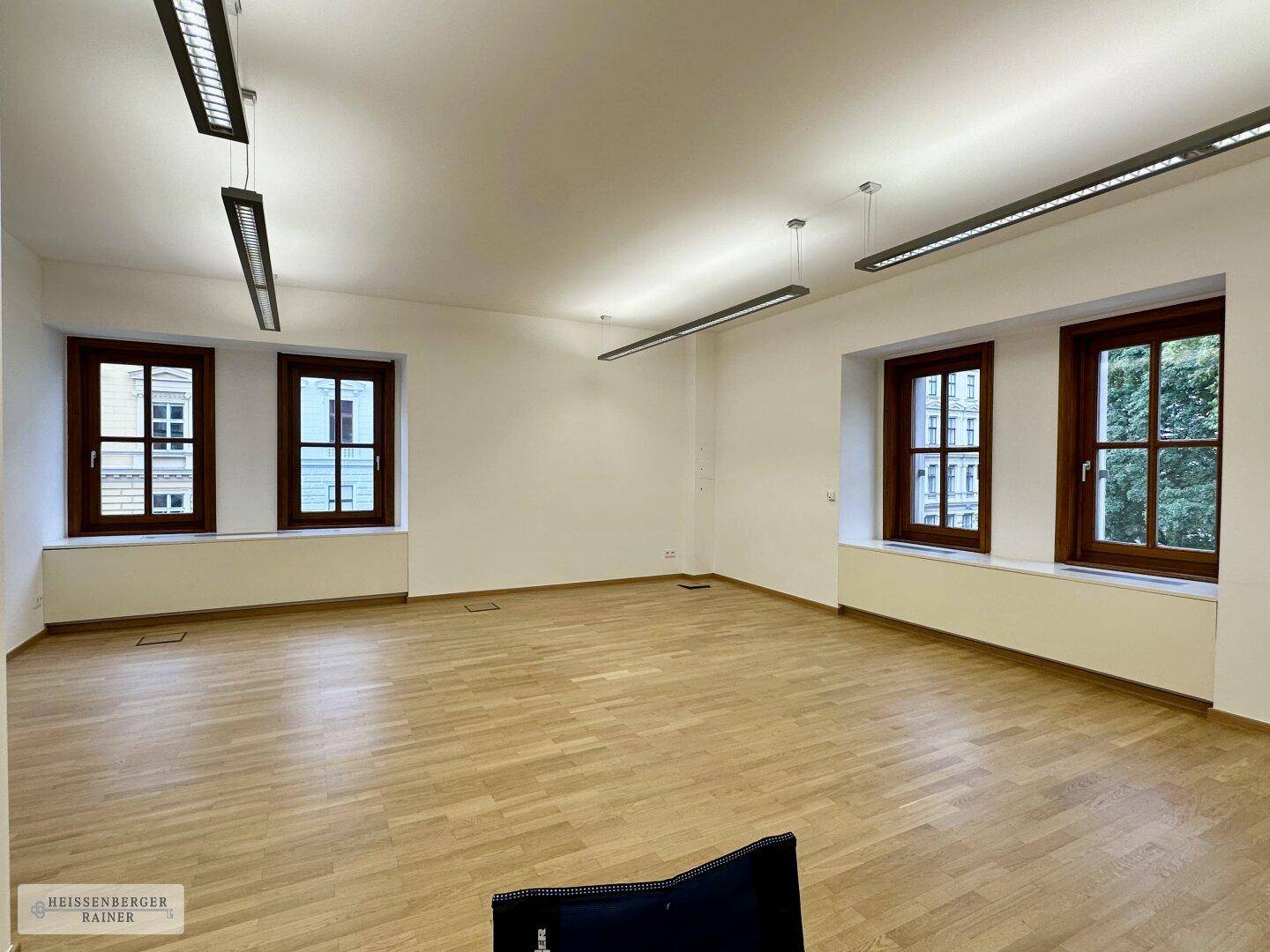 Geräumiger, leerer Büroraum mit Holzboden und großen Fenstern, bereit zur individuellen Gestaltung.