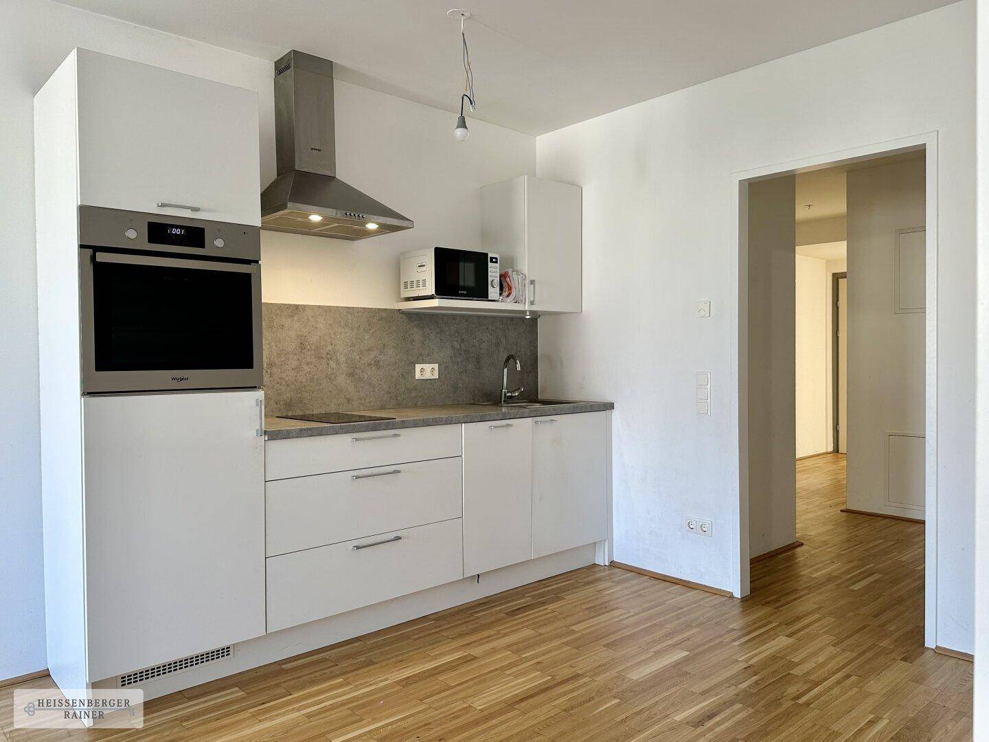 Moderne Einbauküche mit weißen Fronten, integriertem Backofen und Dunstabzugshaube.