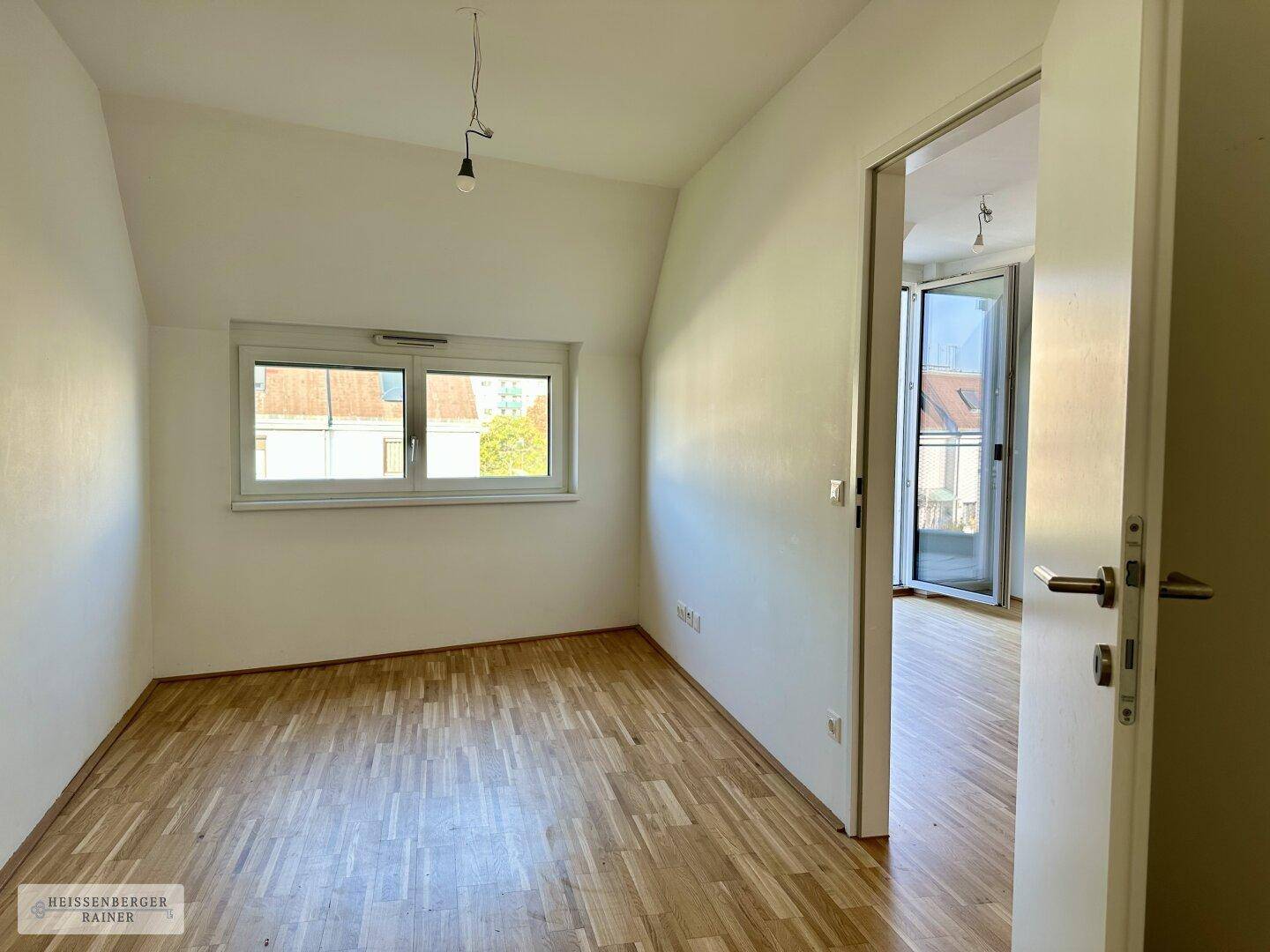 Helles Zimmer mit Parkettboden, Dachschräge und Fenster mit Blick ins Grüne.