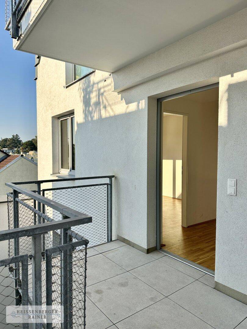 Heller Balkon mit Fliesenboden und Schiebetür, die direkten Zugang zum Innenbereich bietet.
