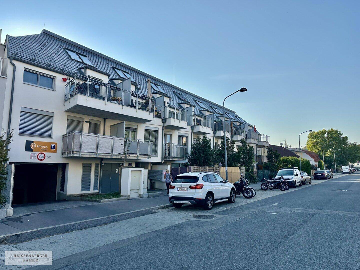 Ansicht eines modernen Wohngebäudes von der Straße mit Balkonen und Parkmöglichkeiten.