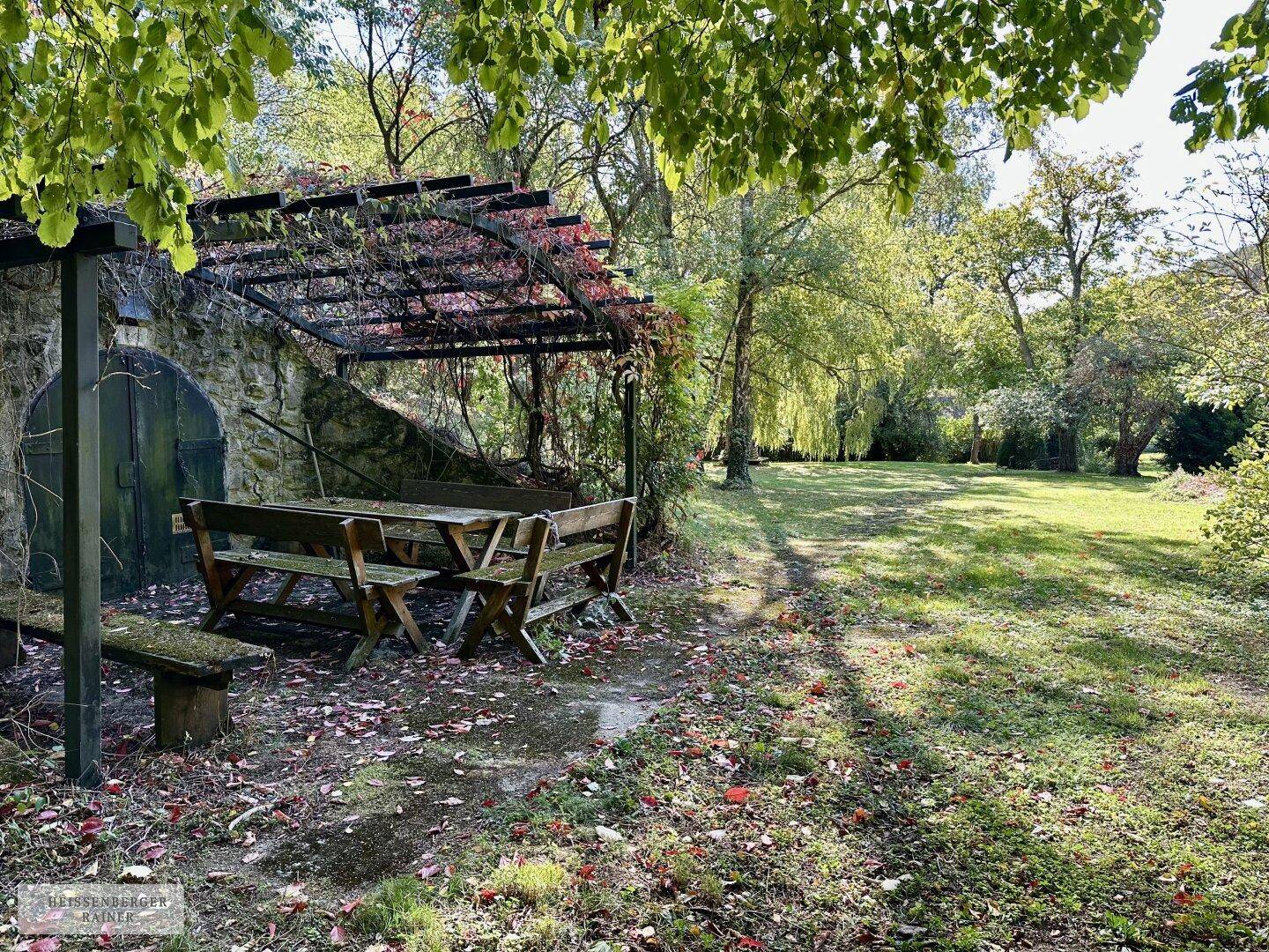 Gemütlicher Außenbereich mit Holzbänken und Tisch unter einer Pergola, ideal für gesellige Stunden.