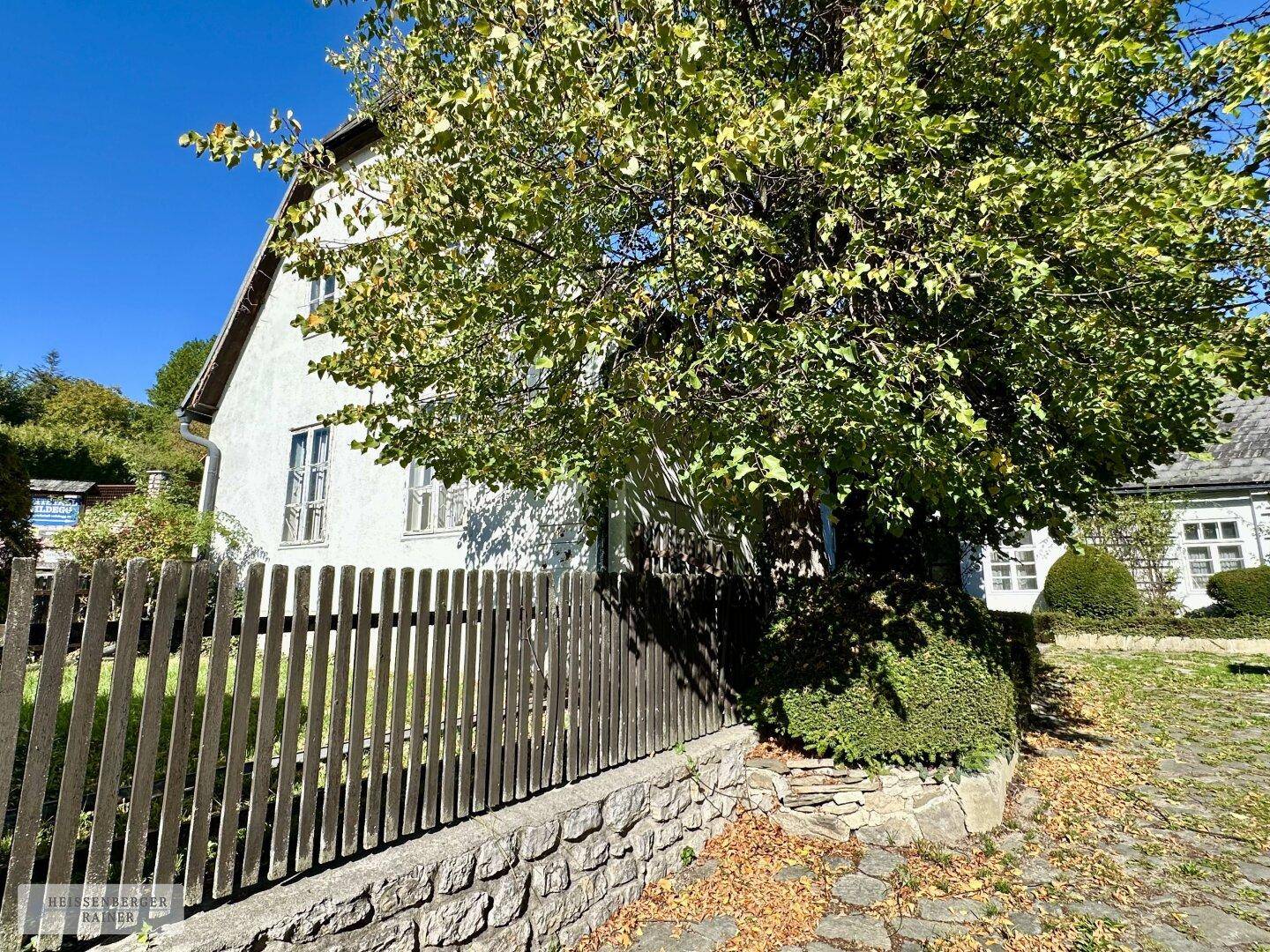 Seitenansicht eines traditionellen Hauses mit weißer Fassade, Holzzaun und altem Baum.