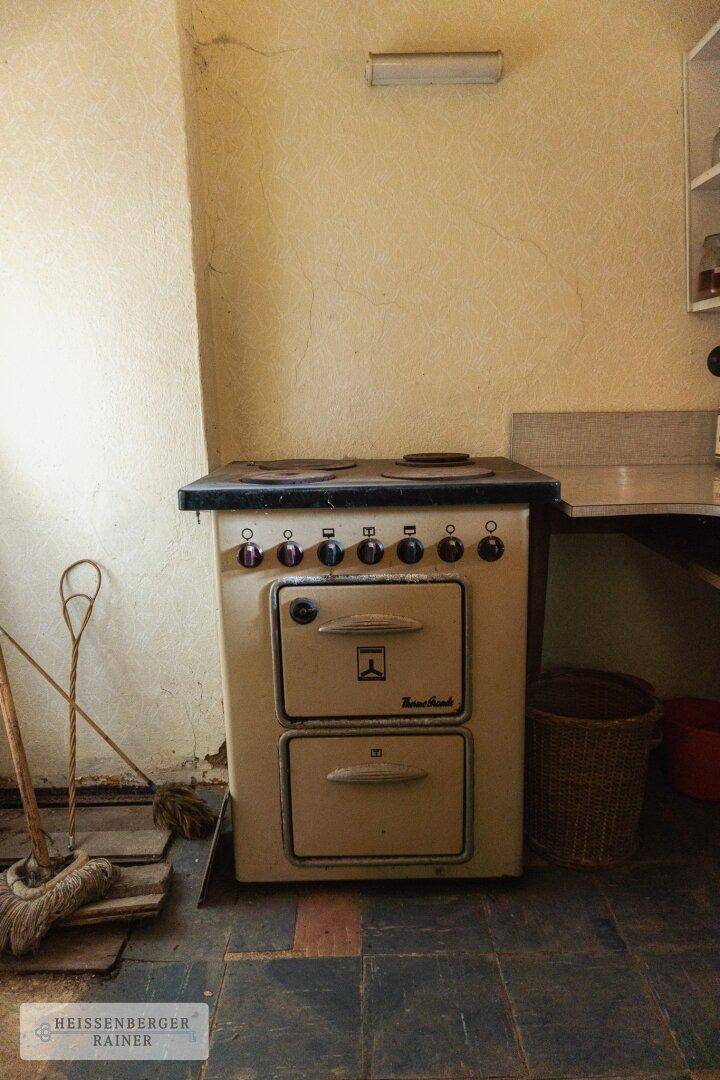 Alter, freistehender Herd mit Backofen in einer einfachen Küche, umgeben von Fliesenboden.