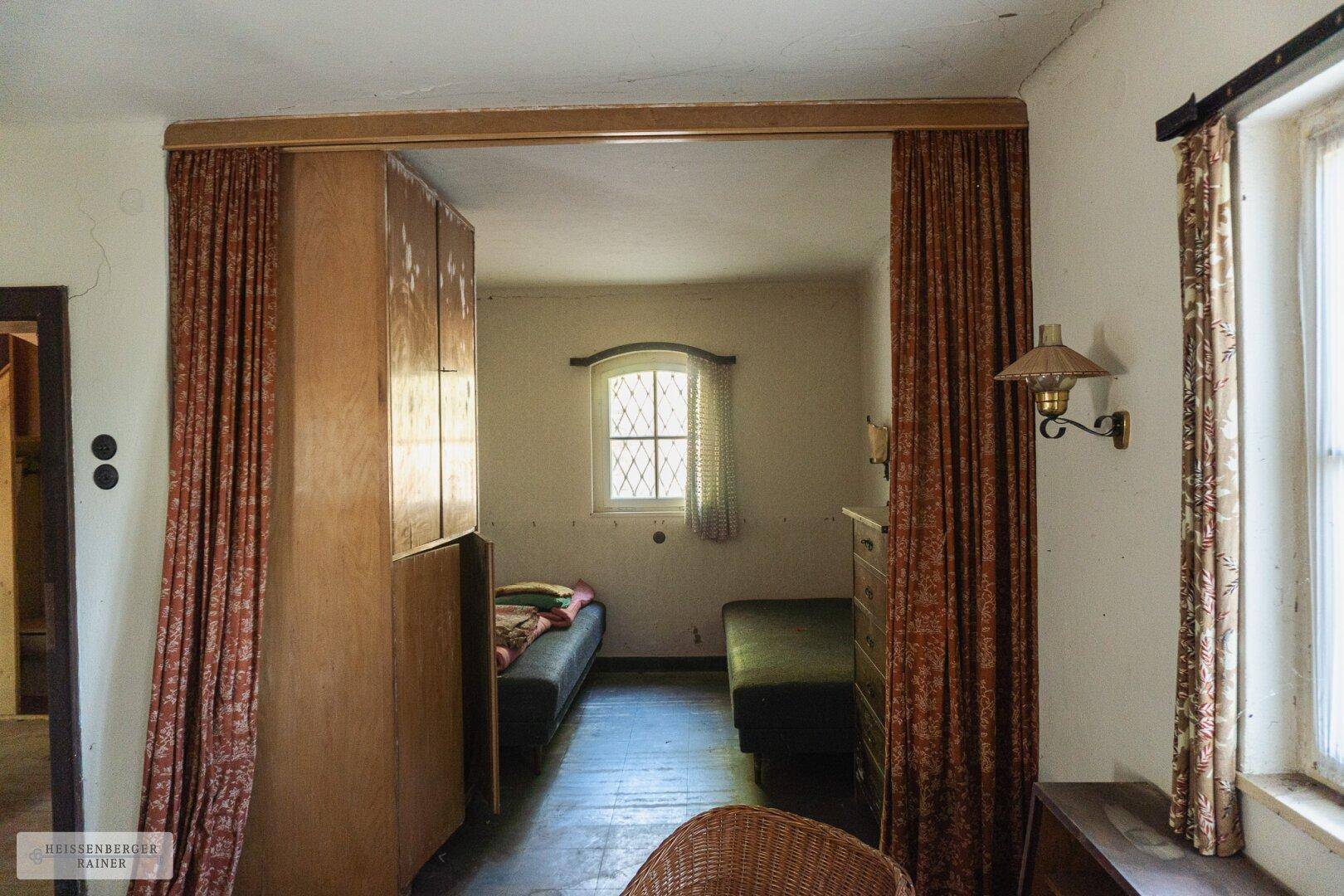 Schlafzimmer mit zwei Einzelbetten, kleinem Fenster und Vorhängen, die den Raum abtrennen.