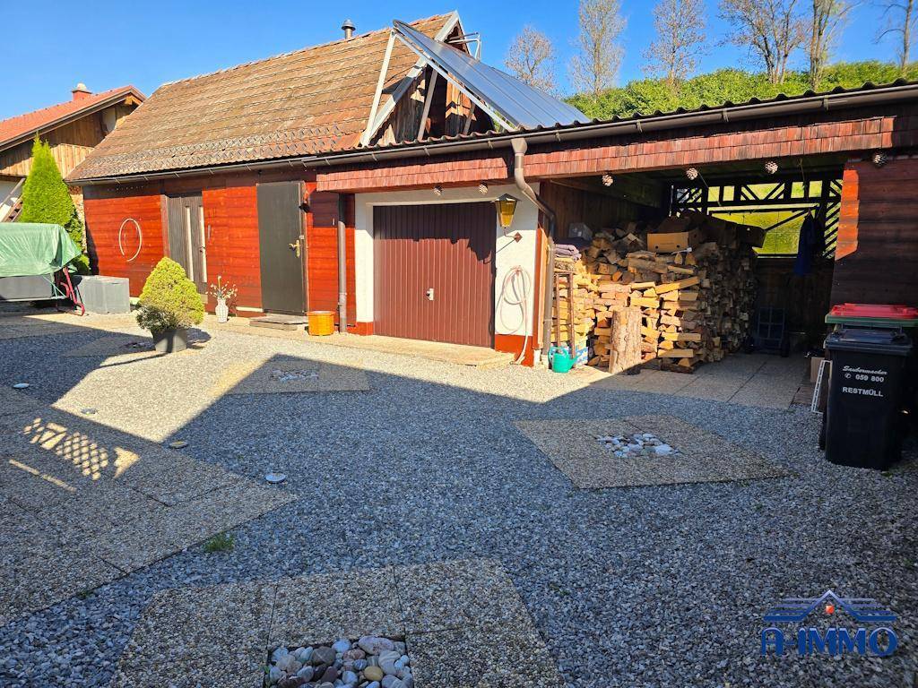 Garage und Holzschuppen mit Brennholzstapel auf dem Kiesvorplatz.