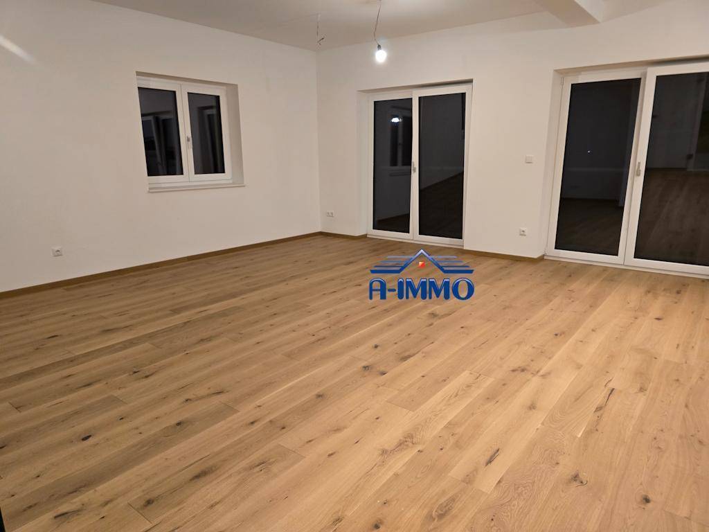 Heller Wohnraum mit Holzboden und großen Fenstern, die viel Tageslicht hereinlassen.