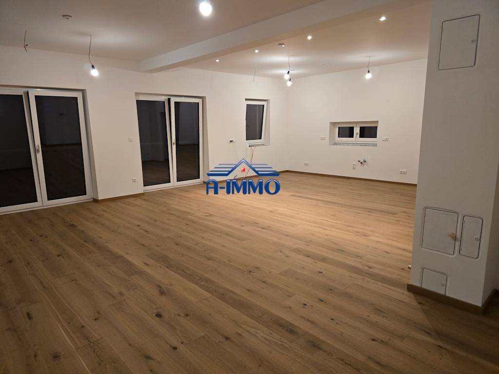 Geräumiges Wohnzimmer mit neuem Holzboden und großen Schiebetüren zum Außenbereich.