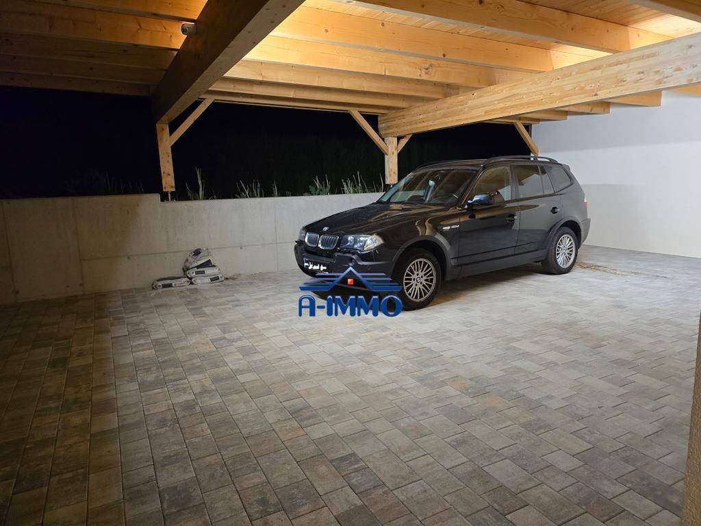 Überdachter Carport mit gepflastertem Boden und Holzbalkenkonstruktion, bietet Schutz für Fahrzeuge.