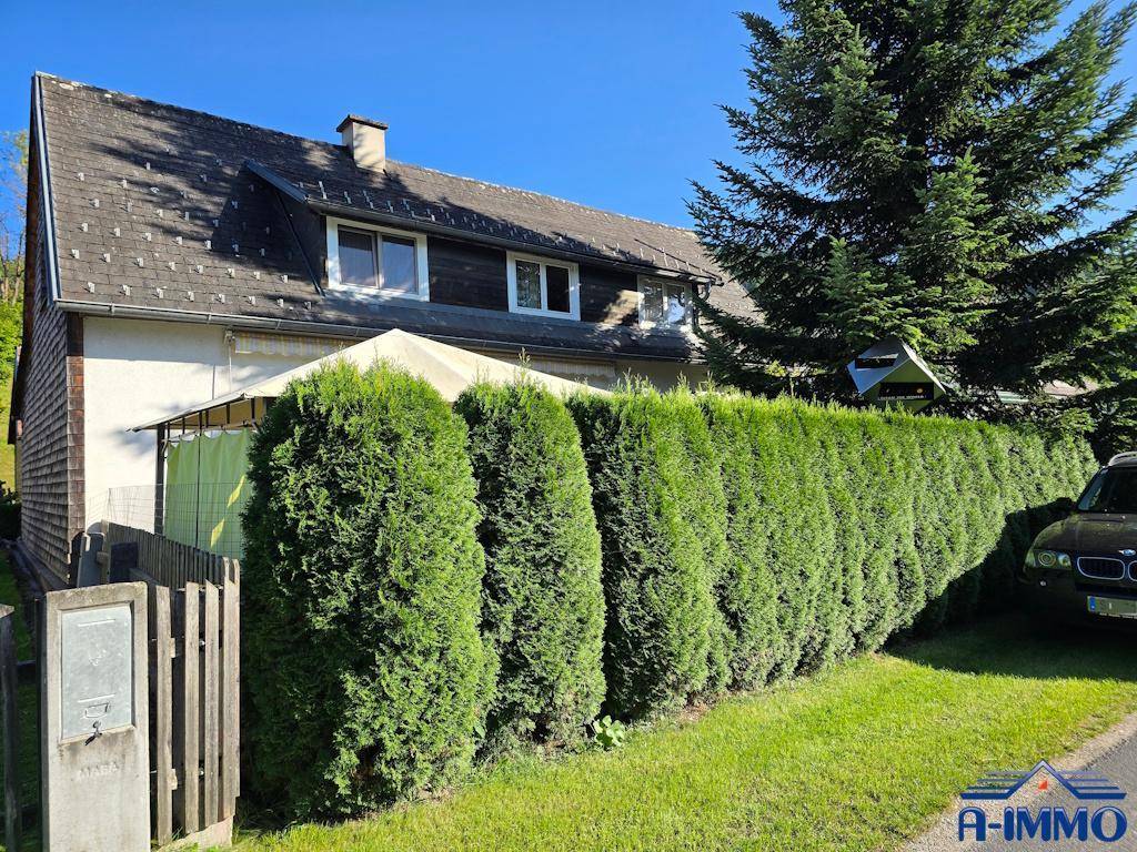 Hausfassade mit Satteldach und hoher Hecke, die Privatsphäre bietet.