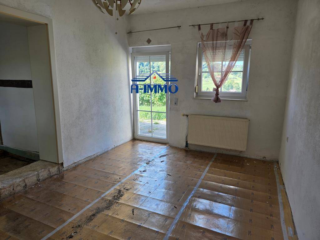 Heller Raum mit vorbereitetem Boden, weißen Wänden und einer Glastür zum Außenbereich.