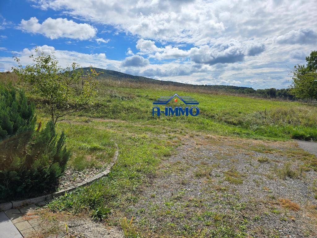 Kiesfläche neben einer grünen Wiese mit sanften Hügeln im Hintergrund unter blauem Himmel.
