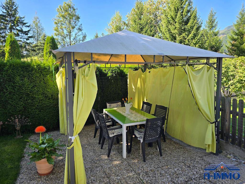 Gemütlicher Pavillon im Garten mit Esstisch und Stühlen, umgeben von grüner Hecke.