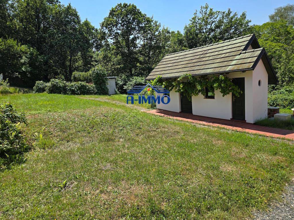 Kleines Nebengebäude im Gartenbereich, umgeben von Rasen und Bäumen.