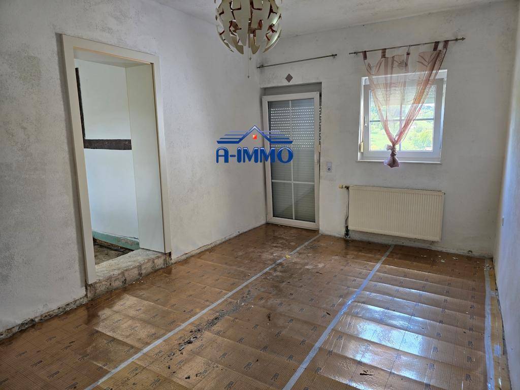 Helles Zimmer mit vorbereitetem Boden, weißen Wänden und einem Fenster mit Vorhang.