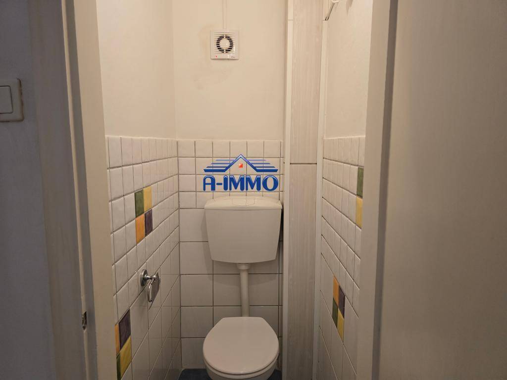 Separates WC mit farbigen Akzentfliesen, Toilette und einem Abluftventilator an der Decke.