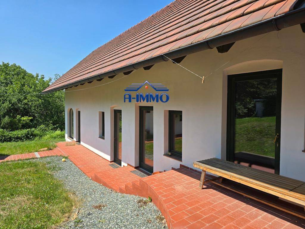 Seitenansicht des Hauses mit mehreren Fenstern, rotem Ziegeldach und einer Holzbank.