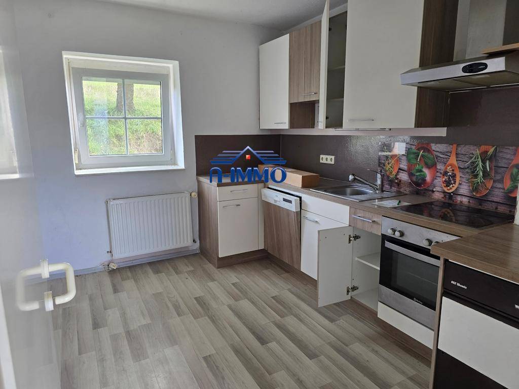 Funktionale Küche mit hellen Holz- und weißen Schränken, Laminatboden und Fenster.