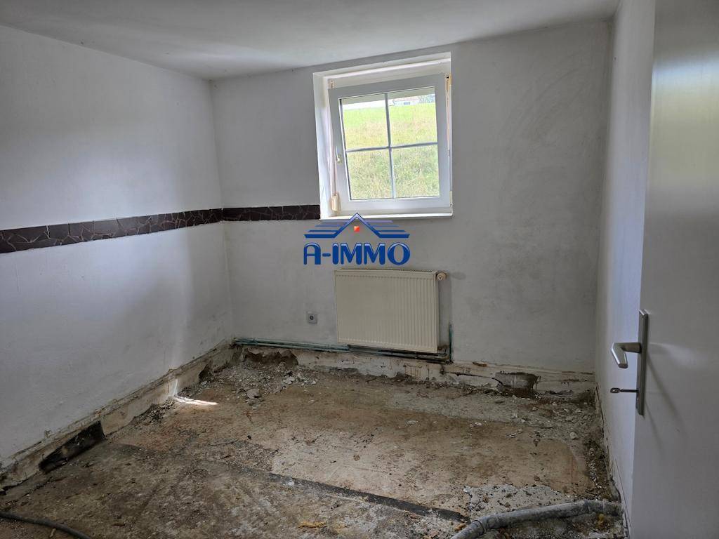 Renovierungsbedürftiger Raum mit Betonboden, teilweise freigelegten Wänden und einem Fenster.