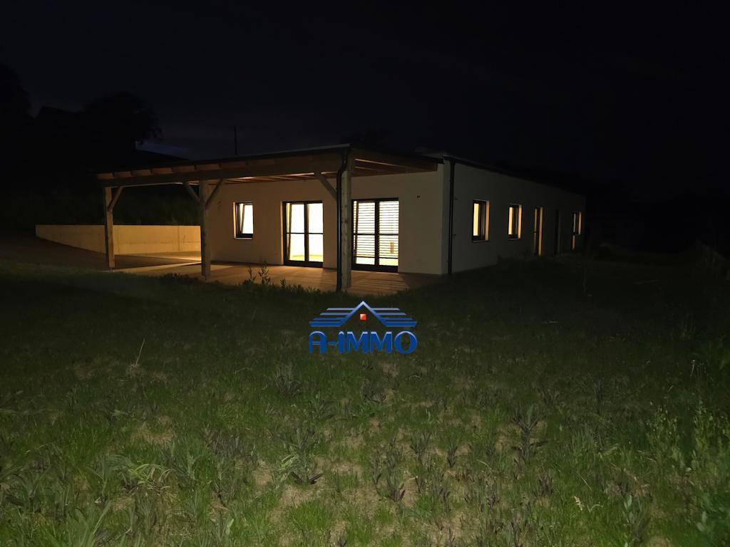 Ansicht des modernen Hauses von der Seite bei Nacht mit beleuchteten Fenstern und Carport.