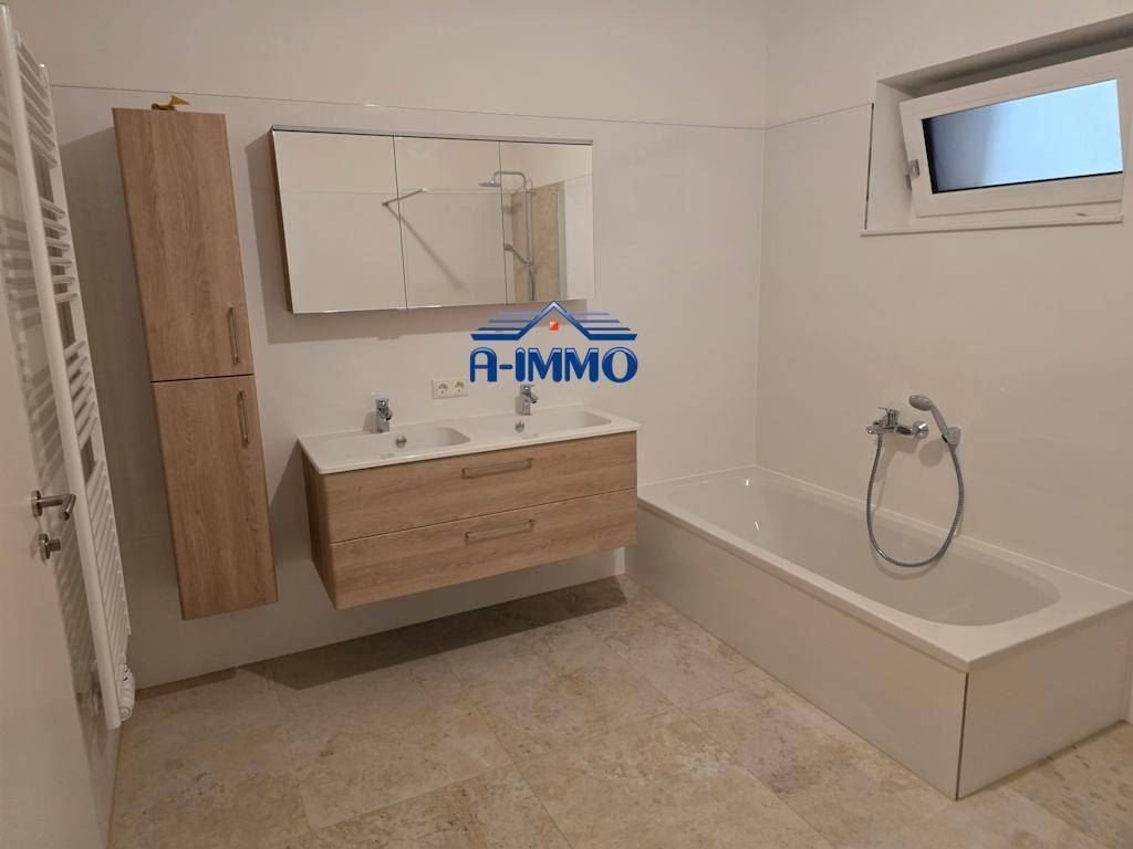 Geräumiges Badezimmer mit Doppelwaschbecken, Badewanne und beheiztem Handtuchhalter.