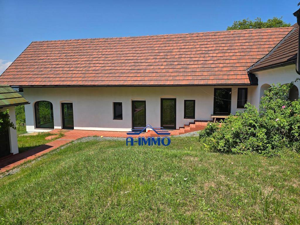 Seitenansicht des Landhauses mit großen Fenstern und einem gepflasterten Bereich im Freien.