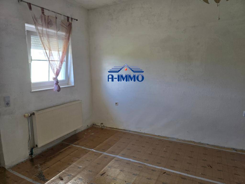 Leeres Schlafzimmer mit vorbereitetem Boden, weißen Wänden und einem Fenster mit Vorhang.