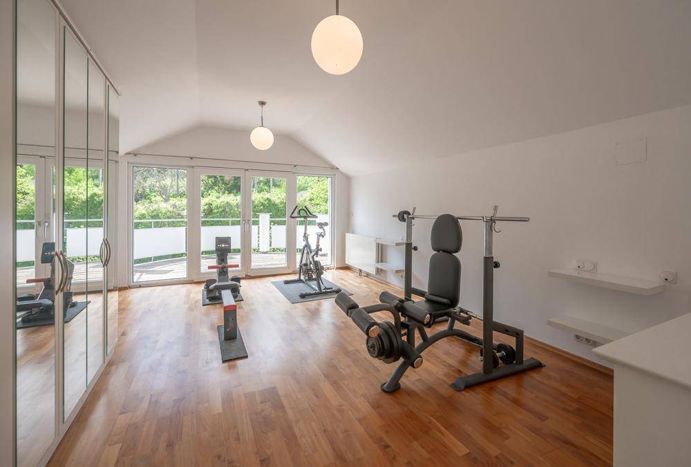 Geräumiger Fitnessraum mit Holzboden, Spiegelfront und Zugang zum Balkon.