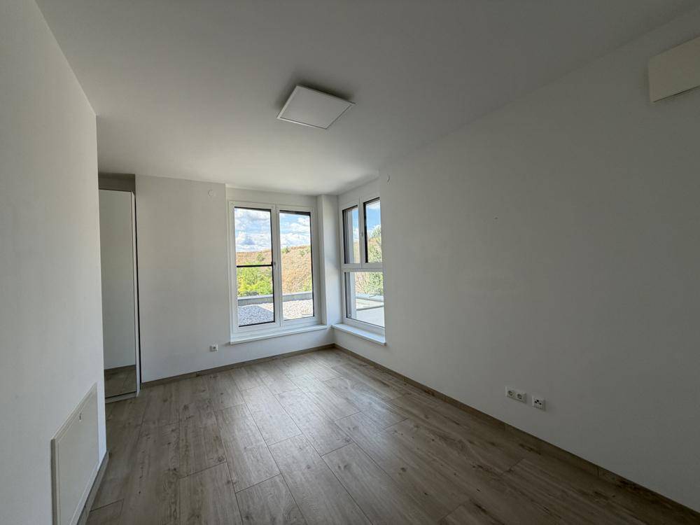 Schlafzimmer mit Holzoptik-Boden, großen Fenstern und Blick ins Grüne.