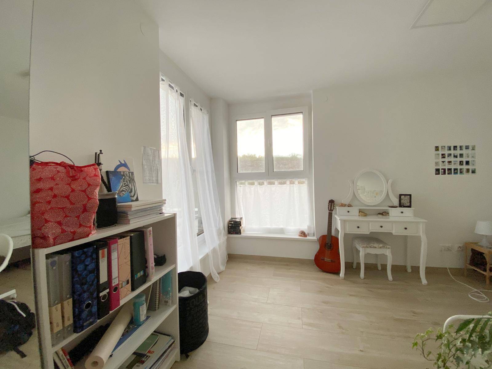 Schlafzimmer mit Bücherregal, Schminktisch und großen Fenstern, die den Raum mit Licht füllen.