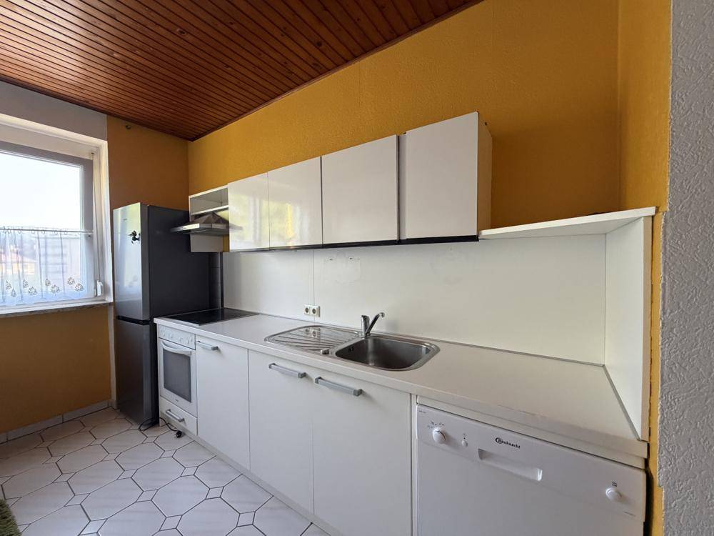 Helle Küche mit weißen Schränken, gelber Wand und Holzdecke, ausgestattet mit modernen Geräten.