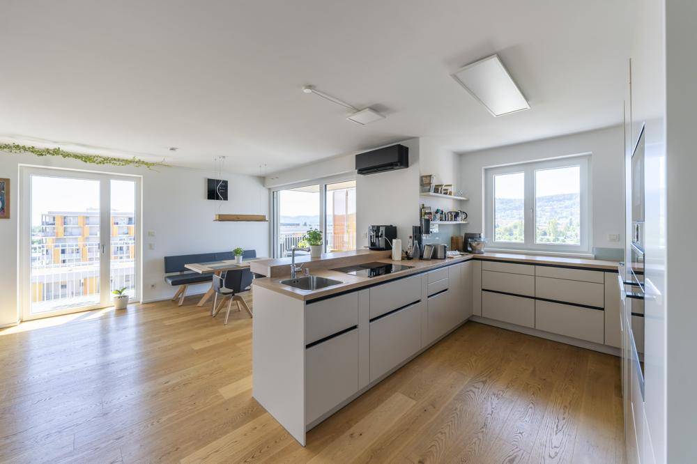 Heller offener Wohn-Essbereich mit moderner Küche, Holzboden und Zugang zum Balkon.