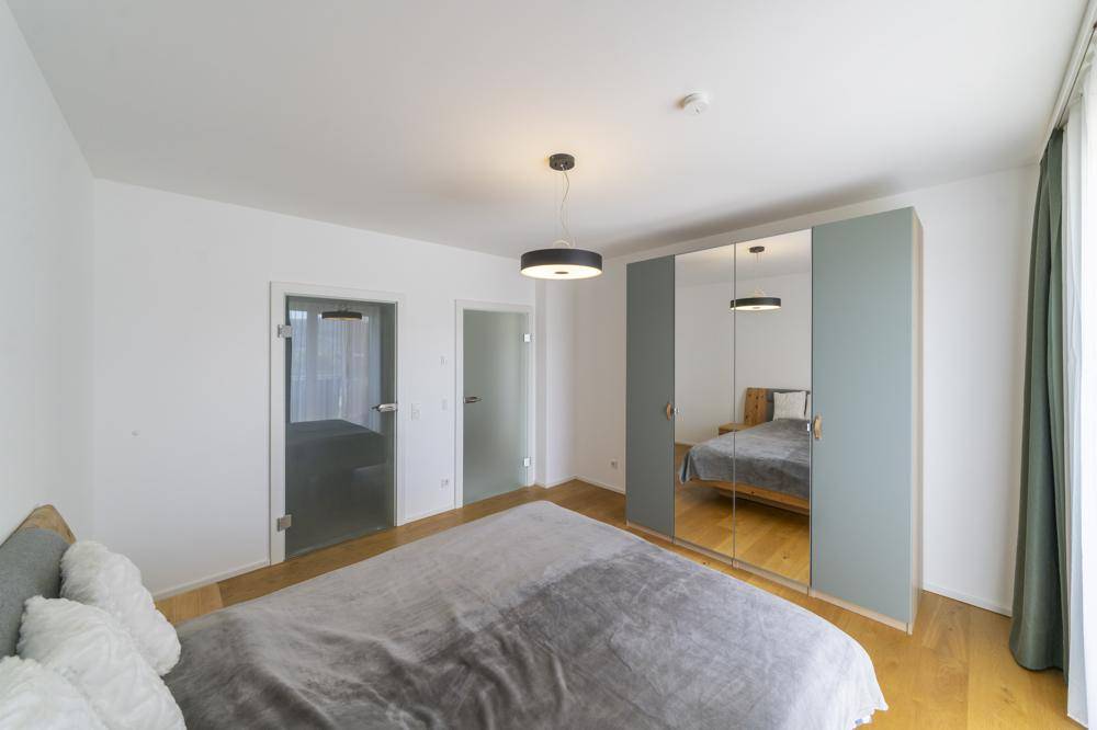 Helles Schlafzimmer mit Holzboden, Spiegelschrank und modernen Glastüren.