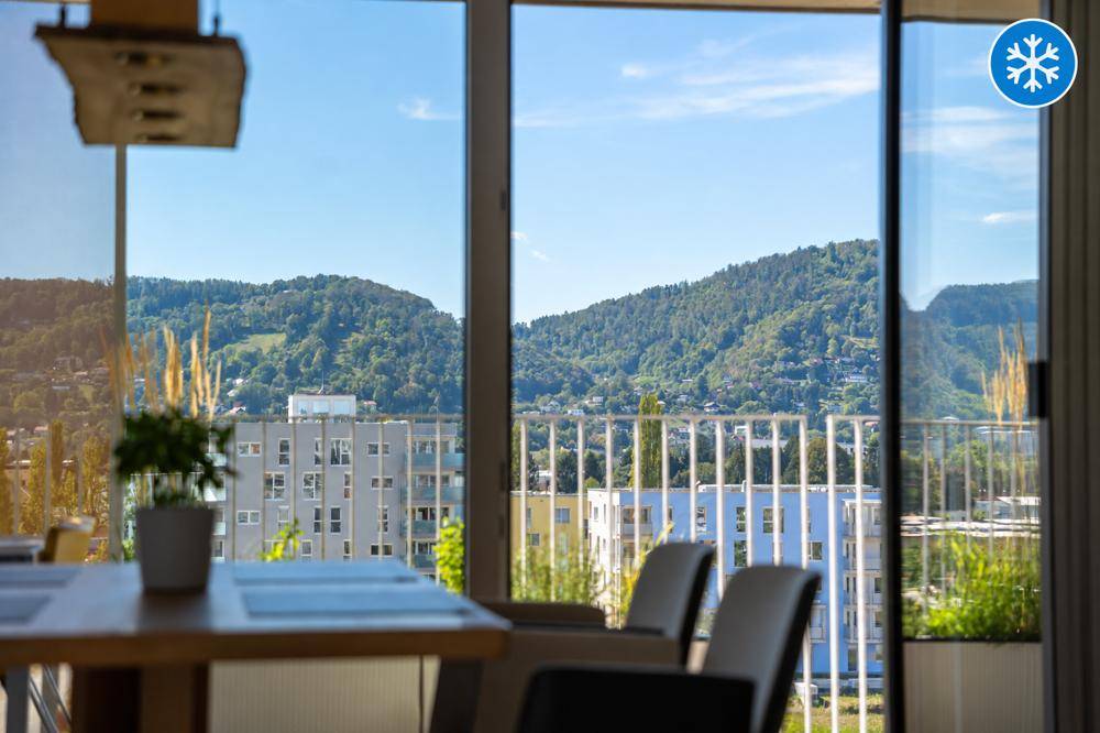 Panoramablick auf die Berge und umliegende Gebäude durch große Fenster vom Essbereich.