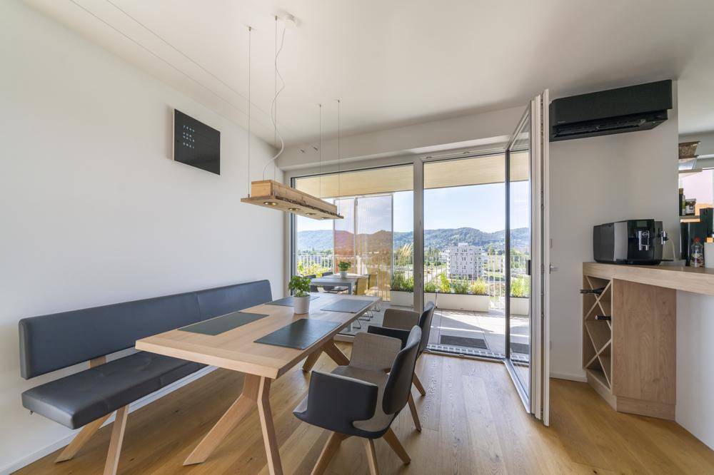 Heller Essbereich mit Holztisch, Sitzbank und Zugang zum Balkon mit Bergblick.