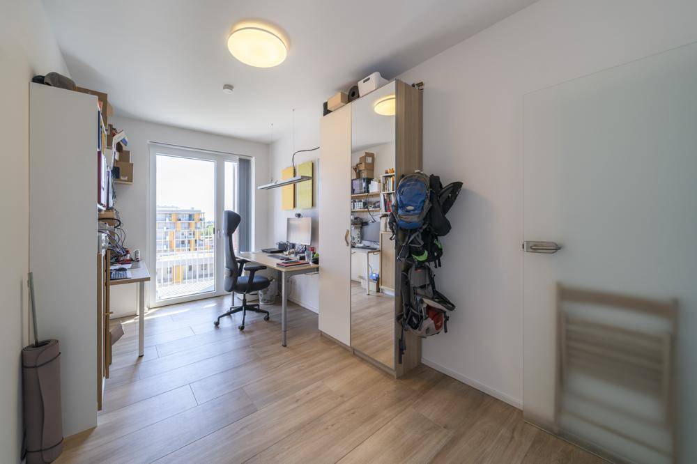 Funktionales Arbeitszimmer mit Schreibtisch, Spiegelschrank und Zugang zum Balkon.