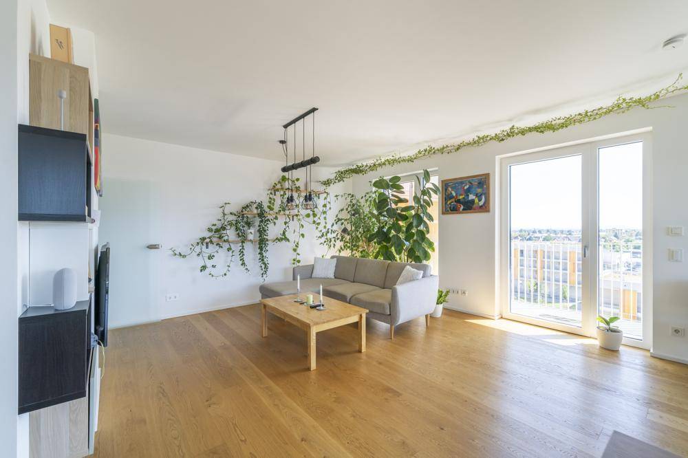 Gemütliches Wohnzimmer mit Holzboden, viel Grünpflanzen und Zugang zu einem Balkon.