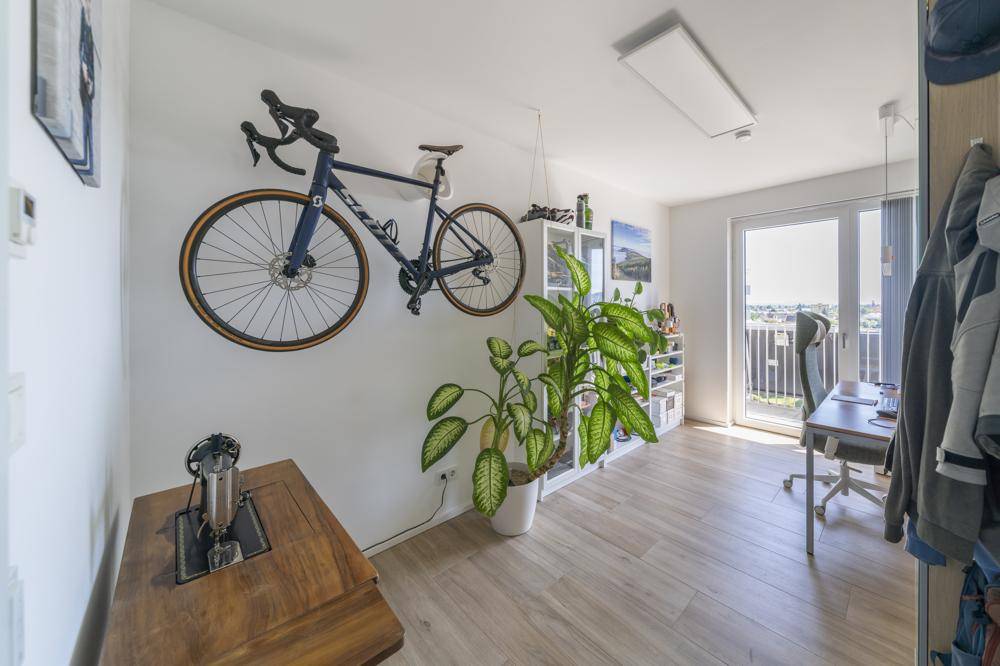 Vielseitiger Raum mit Fahrradhalterung, Schreibtisch und Zugang zum Balkon.