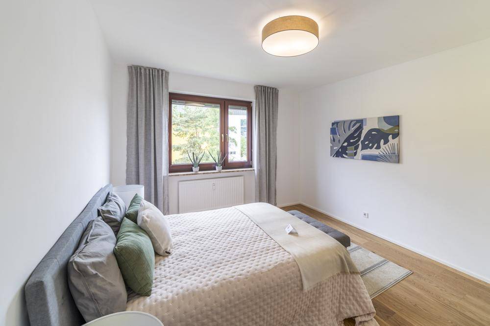 Gemütliches Schlafzimmer mit Doppelbett, Holzboden und Fenster mit Blick ins Grüne.
