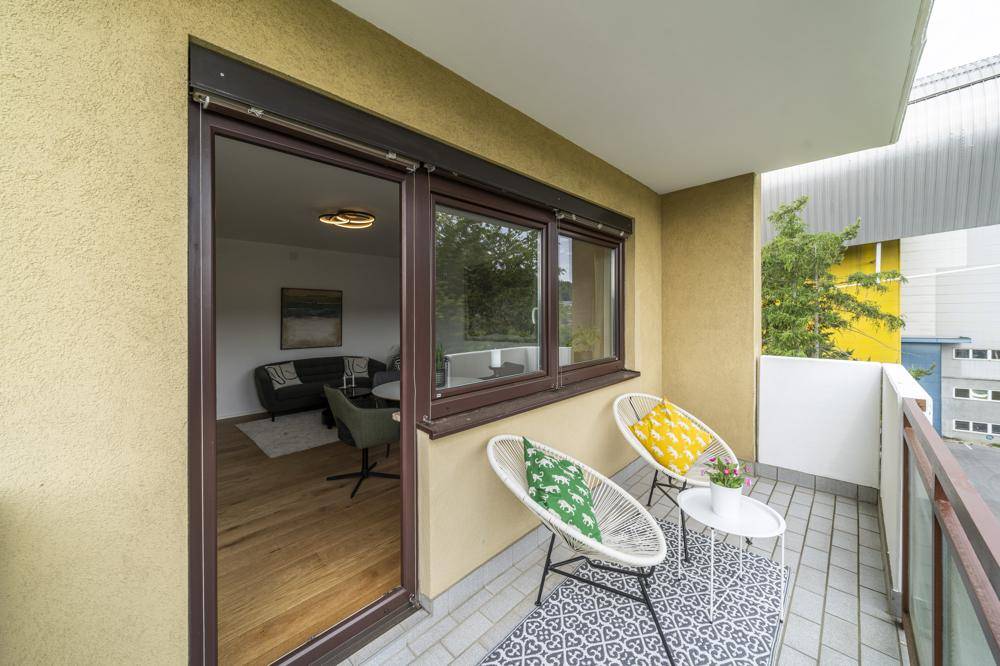 Möblierter Balkon mit Fliesenboden und Blick in den Wohnbereich durch die Glastür.