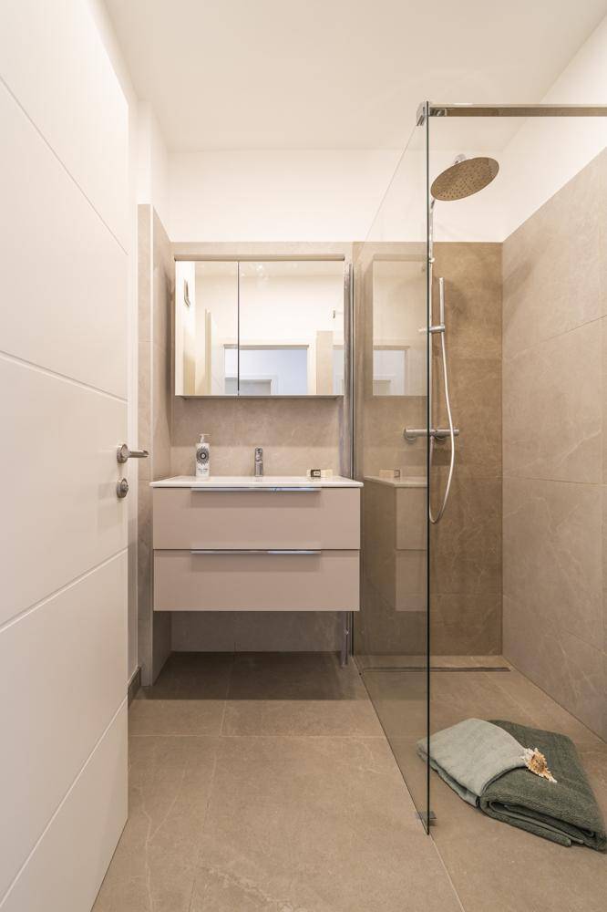 Modernes Badezimmer mit ebenerdiger Dusche, Einzelwaschbecken und Spiegelschrank.