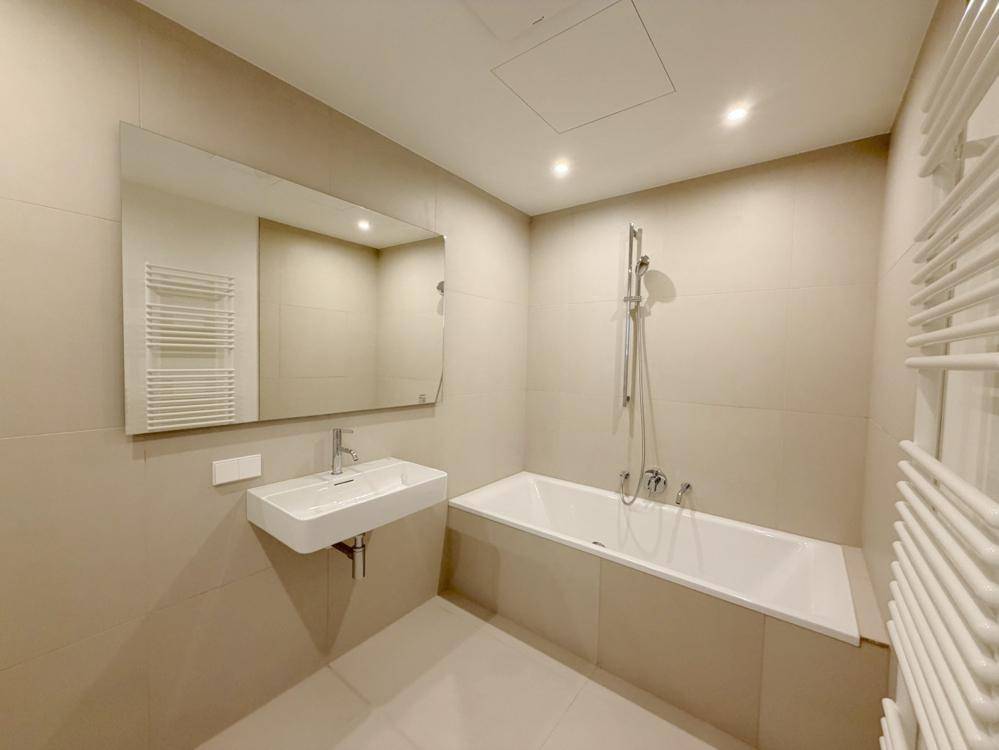 Modernes Badezimmer mit Badewanne, wandhängendem Waschbecken und beheiztem Handtuchhalter in hellen Beigetönen.