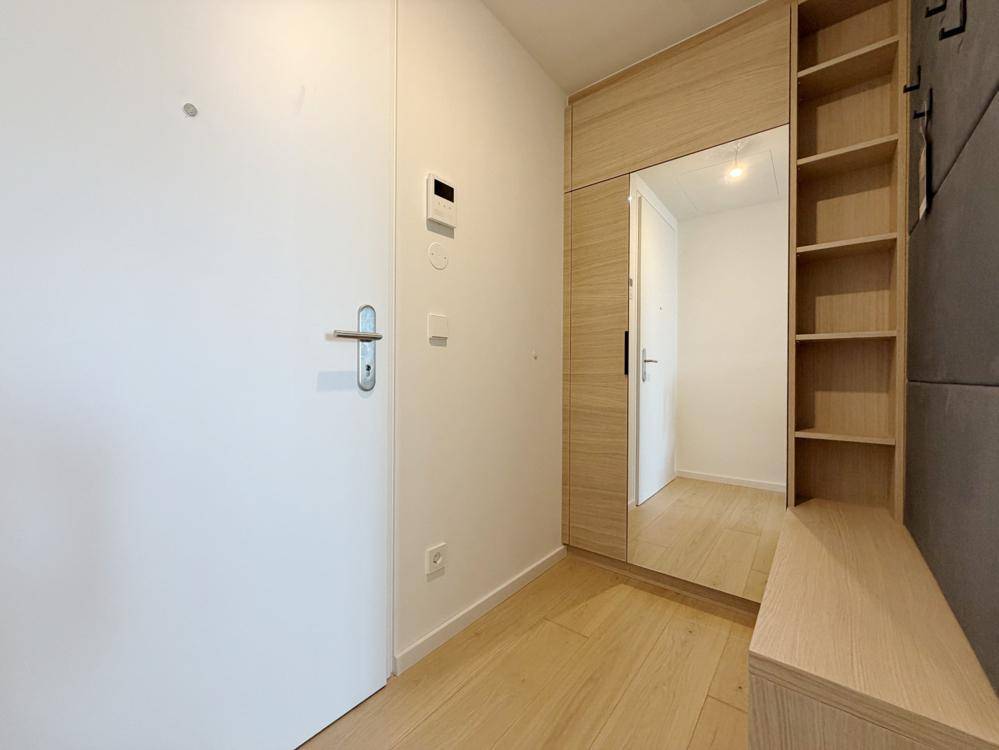 Heller Eingangsbereich mit Holzboden, weißer Tür und praktischer Einbaulösung mit Spiegel und Ablagen.